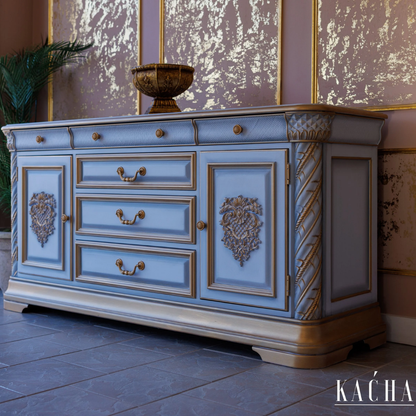 Decorative blue cabinet with gold accents in a room with patterned wallpaper.
