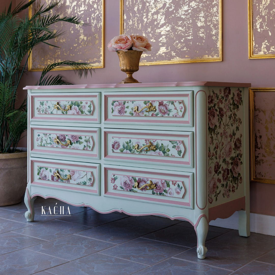 Decorative chest of drawers with floral patterns in a room with pink walls and framed artwork.